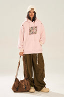 Person wearing a pink hoodie with a floral design, holding a brown bag on a white background