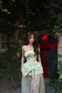 Woman in a Vogsion Pistachio Green Strapless Corset Ruffle Peplum Lace Prom Dress 2026 standing in front of a stone archway with red fabric.