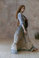 Woman in Vogsion Tiered Pleated Lace-Trimmed Printed Silk Maxi Skirt walking in a room with a stone wall.