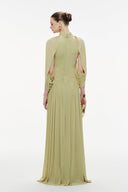 Woman wearing a Vogsion Light Pomelo Olive Mesh Knit Draped Cape Pleated Maxi Dress with cut-out shoulders on a white background