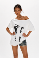 Petite model wearing the VOGSION ÉCLIPSE oversized white off shoulder graphic tee with abstract eye print. Breathable cotton loose fit summer t-shirt designed for petite women with a flattering off shoulder neckline that can also be worn as a boat neck, perfect for casual streetwear, travel, layering and everyday outfits.