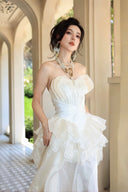 Vogsion Seraphina Royale luxury cream silk gown with peplum lace detailing and tiered skirt, worn by a woman in a Mediterranean villa hallway with classical arches.