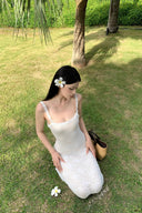 A woman modeling the Vogsion Seraphina white floral lace maxi dress with delicate ruffle straps and a form-fitting mermaid silhouette, perfect for a romantic vacation aesthetic.