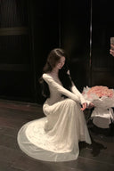 Woman in a white dress sitting on the floor with flowers in a dimly lit room.