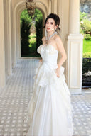 Vogsion Seraphina Royale luxury cream silk gown with peplum lace detailing and tiered skirt, worn by a woman in a Mediterranean villa hallway with classical arches.