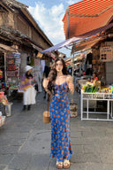 Model wearing cobalt blue maxi slip dress with red floral print and spaghetti straps, styled with a woven bag, perfect summer vacation outfit and chic market day look.