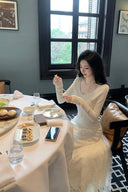 Woman sitting at a table with food and a phone, in a room with a window and decor.