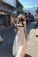 Woman in Vogsion lace-trim ruffle maxi dress and straw hat walking down a street with traditional buildings and mountains in the background.