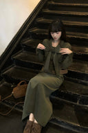 Model wearing moss green corduroy maxi dress with bow tie neckline and belted waist, styled as an elegant autumn long sleeve dress for fall and winter fashion, perfect for city chic and vintage inspired outfit ideas.