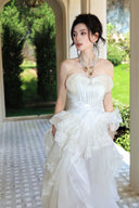 Vogsion Seraphina Royale luxury cream silk gown with peplum lace detailing and tiered skirt, worn by a woman in a Mediterranean villa hallway with classical arches.