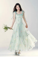Woman wearing a light green floral dress holding flowers against a white background