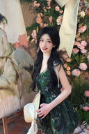 A young woman wearing a French vintage forest green floral dress standing next to a classical oil painting.