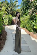 Vogsion Aphrodite Draped Set on a real customer featuring a chocolate brown lace-up corset top and moss green low-waist maxi skirt with hip cut-outs in a tropical resort setting.