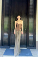 Vogsion Aphrodite Draped Set on a real customer featuring a chocolate brown lace-up corset top and moss green low-waist maxi skirt with hip cut-outs in a tropical resort setting.