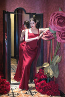 Woman in a Vogsion Amara Wine Red Square Neck Maxi Dress standing next to a mirror with flowers around her.