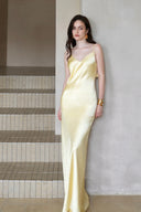 Vogsion Butter Yellow Satin Backless Slip Maxi Dress with Rosette Detail – front view leaning pose showing V neckline and sleek fit