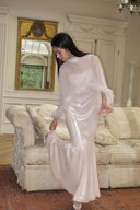 Woman in a Vogsion Blush Feather-Trim Sequin Maxi Evening Gown standing in a room with a mirror and sofa.