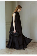 Woman in a black dress holding a matching clutch in a minimalistic setting