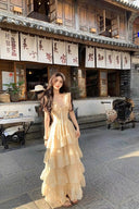A woman wearing the Vogsion champagne tiered ruffle maxi dress standing in front of a traditional vintage wooden building.