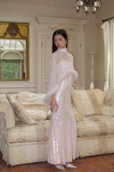 Woman in a Vogsion Blush Feather-Trim Sequin Maxi Evening Gown standing in a living room with a chandelier and mirror.