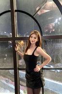 Woman in a Vogsion black corset draped mini dress standing in front of a glass door with reflections.