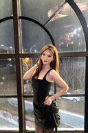 Woman in a Vogsion black corset draped mini dress standing in front of a large window with reflections.