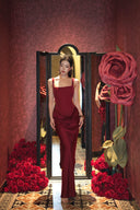 Woman in a Vogsion Amara Wine Red Square Neck Maxi Dress standing in front of a mirror with red flowers around.
