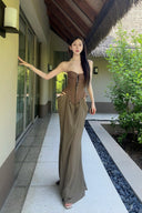 Vogsion Aphrodite Draped Set on a real customer featuring a chocolate brown lace-up corset top and moss green low-waist maxi skirt with hip cut-outs in a tropical resort setting.