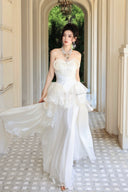 Vogsion Seraphina Royale luxury cream silk gown with peplum lace detailing and tiered skirt, worn by a woman in a Mediterranean villa hallway with classical arches.