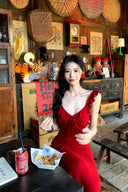 Vogsion real customer (not a professional model) wearing the Poppy Red Ruffle Maxi Dress in a rustic scenic setting — body-hugging red maxi dress with ruffle straps and plunging V-neckline