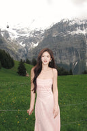 Woman in a pink dress standing in a grassy field with mountains in the background