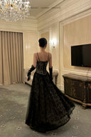 Woman in a black evening gown standing in an elegant room with a chandelier and television.