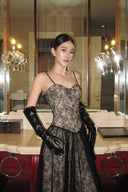 Woman in a black lace dress and gloves standing in a room with mirrors and chandeliers.