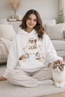 Woman wearing a hoodie with cat illustrations sitting on the floor with a cat in a living room.
