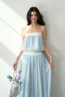 Woman wearing a light blue and white dress holding flowers indoors.