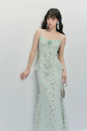 Woman wearing a light green strapless dress with floral details against a white background