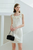 Woman wearing a white dress with floral details holding a black handbag indoors.