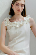 Woman wearing a white dress with floral embellishments against a plain background