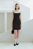 Woman wearing a black dress with white floral details in a minimalistic setting