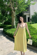 Woman in a yellow dress standing outdoors with greenery and a building in the background