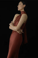 Woman in a rust-colored dress standing against a black background