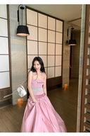 Woman in a pink dress standing in a room with wooden paneling and a lamp.