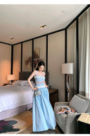 Woman in a light blue dress standing in a modern bedroom.