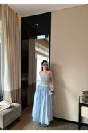 Woman in a light blue dress standing in a room with a large mirror.