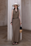 Woman wearing sleeveless olive brown cowl neck maxi dress with a black braided belt and straw bag