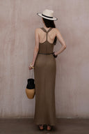 Full-body shot of model in olive brown draped neck maxi dress styled with wide-brim hat and black sandals