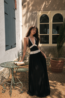 Model wearing VOGSION Riviera Muse plunging halter backless maxi dress in a European village, featuring gold button accents and luxury cruise-inspired styling.