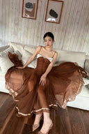 A woman wearing a The Vogsion Liane Petite Wedding Guest Organza Ruffle Midi Dress with a sweetheart neckline and a voluminous pleated skirt, sitting on a white sofa in a room with wood-paneled walls.