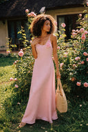 Model in the Vogsion Last Sunset Rosette Linen Slip Dress posing in a blooming rose garden, blush pink linen slip maxi dress with floral rosette accent, elegant wedding guest dress, European summer outfit, feminine vacation style, breathable linen clothing, luxury resort fashion.