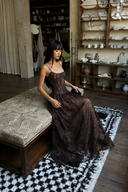 Woman in Vogsion Mara Maxi Dress sitting on a patterned rug in a room with shelves and decor.